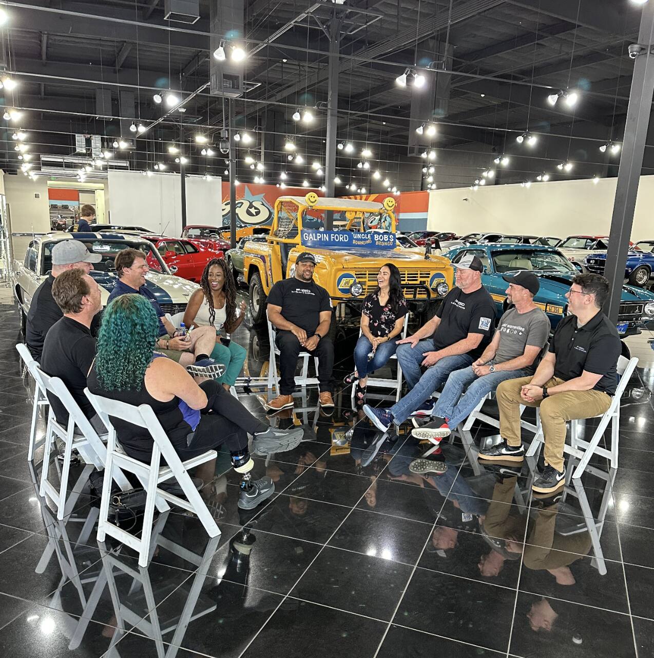 Jim Farley meets with a group of EV enthusiasts and advocates at Galpin Auto Sports. They are seated in a circle and smiling.
